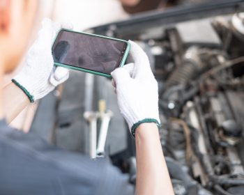 Hand of car mechanic or technician holding smartphone taking photography of car engine open hood. Car service concept.